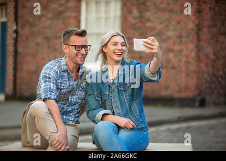 Eine Frau, eine selfie mit einem Mann, während Sie auf einer Bank sitzen. Stockfoto