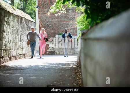 Eine Vorderansicht Schuß von drei Geschäftsleute in einer Straße der Stadt. Zwei sind, halten sich an den Händen und laufen in Richtung der Kamera, während ein anderer Mann leicht Spaziergänge behi Stockfoto