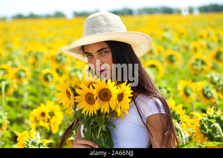 Portrait einer jungen schönen Mädchen in einem Strohhut und mit einem Strauß Blumen in einem Feld mit Sonnenblumen Stockfoto