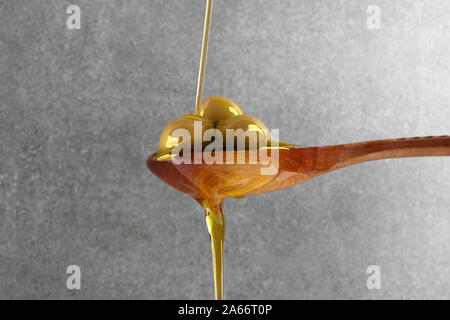 Natives Olivenöl fließt auf einer hölzernen Löffel voller grüner Frische Oliven Stockfoto