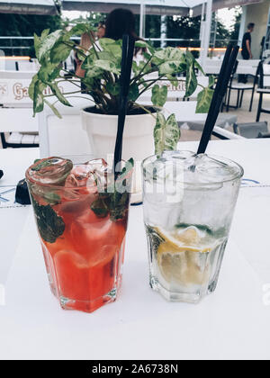 Zwei Gläser gekühlte Limonade mit Zitrone, Minze Blütenblätter, Eiswürfel und Erdbeeren auf einem Glastisch im Sommer in einem Cafe Stockfoto