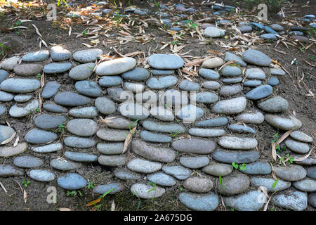 Ein Tuberkel mit glatten Kanten, die Wand ist mit großen Kieselsteinen ausgekleidet. Große Steine auf die Erde im botanischen Garten zu stärken. Stärken Stockfoto