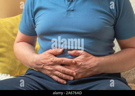 Ein Mann im blauen T-Shirt hält seine Hände auf seinen Magen Stockfoto