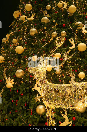 Beleuchtete LED-String Gold Rentier mit einem großen Weihnachtsbaum im Hintergrund Stockfoto