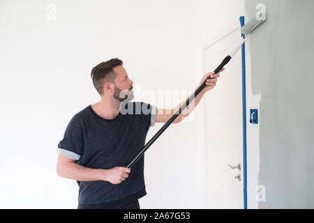Mann rolling hellgrau Farbe auf Wand Stockfoto