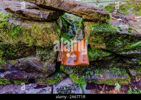 Abfluss Abfluss von einem Teich in einen Abfluss auf einem Stein Straße mit einem bemoosten Felsen Zaun, Tag zu Beginn des Herbstes, Niederlande Holland Stockfoto