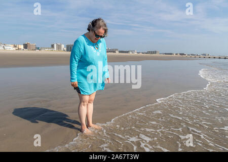 Eine ältere Frau, die sich zu Fuß in den Sand am Strand durch das Meer. Stockfoto