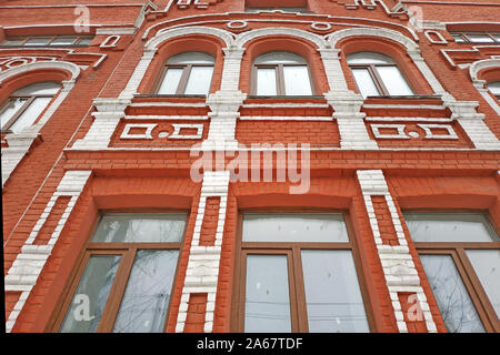 Schöne rote Backsteingebäude mit weißen Zierleisten. Fassade eines alten Hauses. Wand mit Fenstern und Bögen von einem alten Haus, Ansicht von unten. Stockfoto