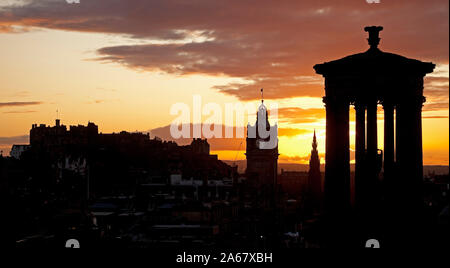 Calton Hill, Edinburgh, Schottland, Großbritannien. 24. Oktober 2019. Farbenfroher Sonnenuntergang über der Innenstadt eine Silhouette von Dugald Stewart Monument und schloss mit Balmoral Hotel im Zentrum. Stockfoto