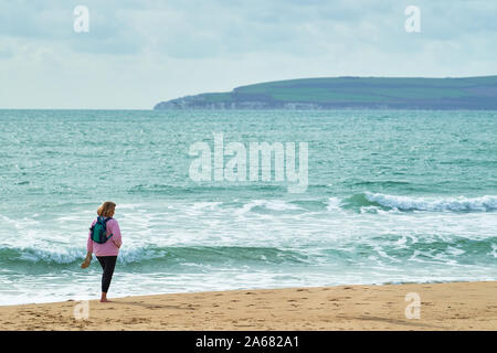 Eine einsame Frau geht barfuß entlang der Küstenlinie von einem Sandstrand neben dem Englischen Kanal in Bournemouth, England. Stockfoto