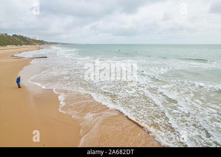 Ein einsamer Mann steht am Ufer und blickt auf die Flut an einem Sandstrand auf den Ärmelkanal in Bournemouth, England. Stockfoto