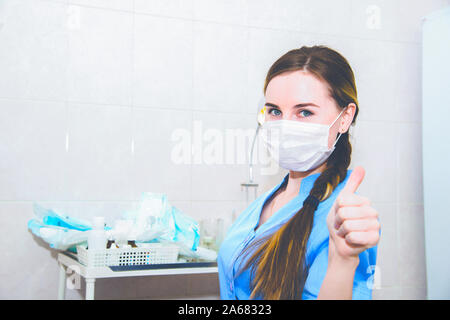 Ärztin in der Maske Frau zeigen Daumen hoch, Handzeichen mit Krankenhaus Hintergrund Stockfoto