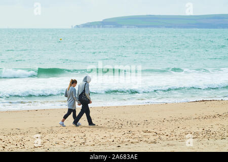 Ein junges Paar gehen Hand in Hand entlang der Küstenlinie von einem Sandstrand neben dem Englischen Kanal in Bournemouth, England. Stockfoto