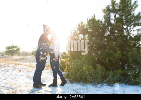 Der Mann mit dem Mädchen küssen im Winter im Wald vor dem Hintergrund der fallenden Süßigkeit. Romantische winterliche Atmosphäre. Stockfoto