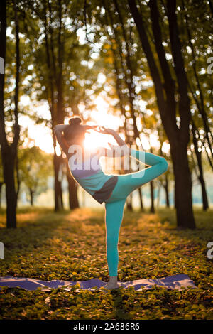 Ein junger Sport Mädchen übt Yoga in einer ruhigen, grünen Wald im Herbst bei Sonnenuntergang, in einem Yoga Asana darstellen. Meditation und Einssein mit der Natur. Stockfoto