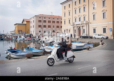 Ein Paar mittleren Alters mit ähnlichen Schuhen fährt eine Vespa entlang der Adriaküste in Piran, Slowenien. Stockfoto