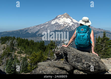 Eine reife Frau Wanderer Websites auf einem Felsen mit dem Rücken zu uns und genießt die Aussicht auf den Mt. Haube von Lookout Mt. Es ist ein strahlend blauer Himmel und hellen Sommer Stockfoto