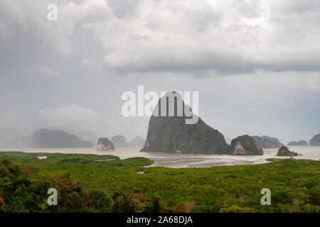 Schöne hohe Klippen, bewachsen mit Bäumen im Meer bei regnerischem Wetter und Regen Wolken im Himmel. Grünen Wald unten. Düster. Stockfoto