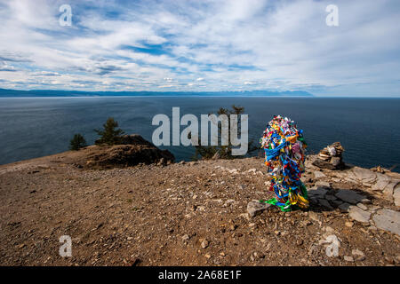 Blick auf den Baikalsee von einer Klippe mit einem Bündel von Bändern auf einer Klippe an einem heiligen Ort auf der Insel Olchon. Wolken im Himmel. Hinter dem Berg Stockfoto