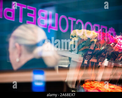 Moskau, Russland - Oktober 19, 2019: Frau mit blonden Haaren wählt Blumen im Store. Foto durch Glas. Blumensträuße der Chrysanthemen und Rosen pric Stockfoto