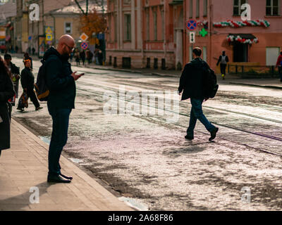 Moskau, Russland - Oktober 19, 2019: ein Mann in einem schwarzen Mantel ist zu Fuß entlang der Straße. Straßenbahn und Menschen stehen an einer Haltestelle. Warme Herbst sonniger Tag. Stockfoto