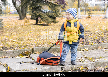 Wenig hooligan Junge gezogen weg Rucksack seiner Mutter und an ihrer im Herbst Stadtpark Grimasse. Stockfoto