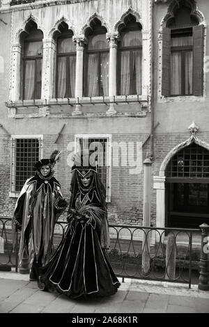 Zwei carnevale Nachtschwärmer in wunderschönen Kostümen Pose vor dem Palazzo Priuli, Fondamenta dell'Osmarin Castello, Venice, Italien. Schwarz und Weiss Stockfoto