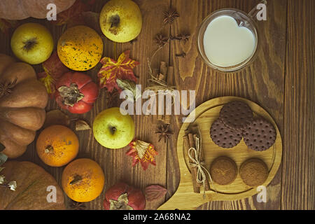 Cookies mit Milch auf den Tisch. Schokolade Kekse und Zimt auf der Holzplatte mit einem Glas Milch und Kürbis mit Apple. Stockfoto