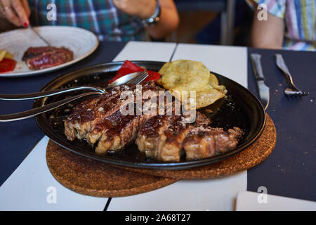Geschnittenes gegrilltes Rindfleisch zum Teilen auf einer heißen Eisenplatte mit Pommes, Terrasse des Restaurante Palomeque, Zaragoza, Spanien Stockfoto