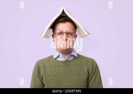 Gelangweilt männlichen Kaukasier Student mit einem Buch auf dem Kopf Stockfoto