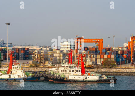 Laem Chabang Seehafen, Thailand - 17. März 2019: Reihen von verankert Schlepper vor Container Yard mit Stapeln und orange Transporter wie Brücken Stockfoto