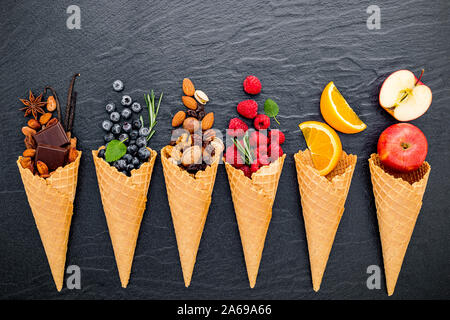 Verschiedene Zutaten für Speiseeis Aromen in Kegel Blueberry, Kalk, Pistazien, Mandeln, Orangen, Schokolade, Vanille und Kaffee auf dunklem Stein bac eingestellt Stockfoto