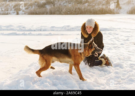 Stilvolle Kerl Spaziergang mit dem Hund. Spaß im Schnee spielen im Freien. Spielerische. Tierliebhaber. Deutscher Schäferhund genießen Sie die Freiheit. Freunde zusammen. Lustig Stockfoto