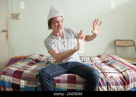 Junger Mann mit Alufolie hat Gefühl im Schlafzimmer Angst Angst Stockfoto