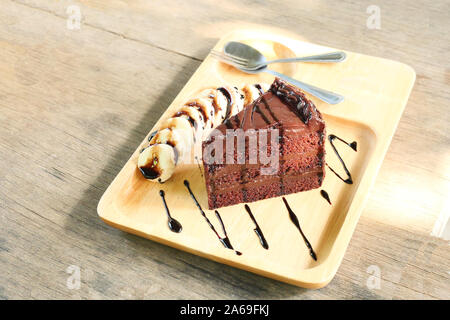 Ein Stück leckeren Schokoladenkuchen mit in Scheiben geschnittenen Banane, süße Speisen mit Löffel und Gabel auf einer Holzplatte mit braunen Tisch im Hintergrund Stockfoto