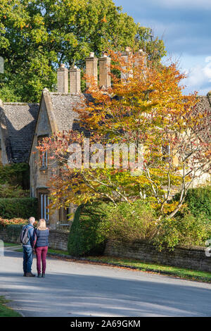 Paar an einer Cotswold Stone House und im Herbst Farben auf einem Baum in Batsford Dorf suchen. Batsford, Moreton-in-Marsh, Cotswolds, Gloucestershire, VEREINIGTES KÖNIGREICH Stockfoto