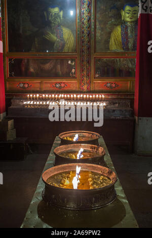 Votive yak Butter Kerzen brennen als Opfergaben vor den Statuen des Buddha in der Coquen Saal des Klosters Ganden auf Wangbur Mountain in Tibet. Stockfoto