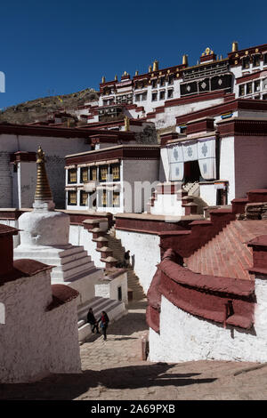 Zwei Besucher durch eine Stupa in den Ganden BuddhistMonastery auf Wangbur Mountain in Tibet als ältere tibetische Frau steigt einige Treppen. Stockfoto