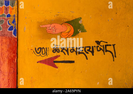 Ein gemaltes Schild mit Wegbeschreibungen und eine Hand auf dem Weg zur Toilette im buddhistischen Kloster Ganden auf Wangbur Mountain in Tibet. Stockfoto