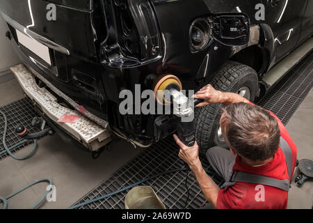 Nahaufnahme auf die Hände eines männlichen Arbeitnehmer, hält ein Werkzeug zum Polieren Sie den Kotflügel eines Autos während der Arbeit in einem Fahrzeug mit Werkstatt. Auto ser Stockfoto