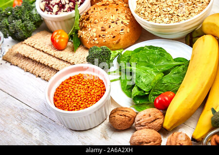 Einstellen der hohen Ballaststoffe Gesundheit Nahrung Produktkonzept mit Obst, Gemüse, Vollkornbrot, Hülsenfrüchten, Getreide, Nüsse und seedson weißen Holzmöbeln hinterg Stockfoto