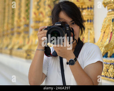 Junge Thai Fotografin hält eine DSLR-Kamera Canon EOS 80D mit beiden Händen vor der Bangkok Wat Chana Songkhram Ratchaworawihan. Stockfoto