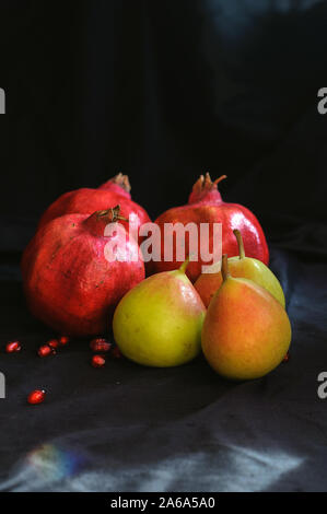 Granatäpfel und Birnen auf einem dunklen Hintergrund und mit verstreuten Granatapfel Samen Stockfoto