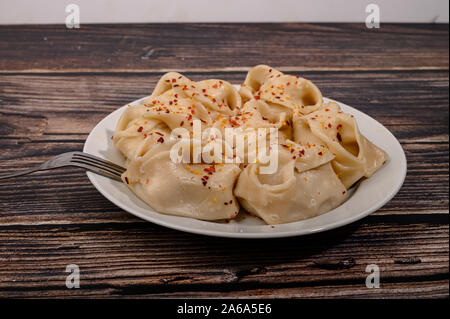 Gekochte manti mit Rindfleisch auf einem Teller mit Gewürze auf einem Holztisch Stockfoto