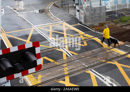 Frau im gelben Mantel Spaziergänge durch eine klare Bahnübergang nach den Barrieren angehoben wurden. Stockfoto