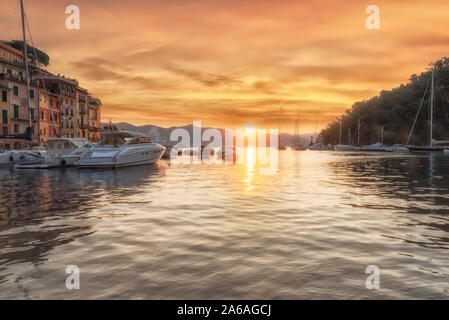 Bunte Sonnenaufgang über Portofino Hafen und Uferpromenade an der italienischen Riviera, Ligurien, Italien an einem bewölkten Tag mit Plätschern des Wassers im Vordergrund. Stockfoto