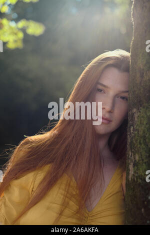 Porträt der rothaarige Junge Frau lehnte sich auf Baum Stockfoto