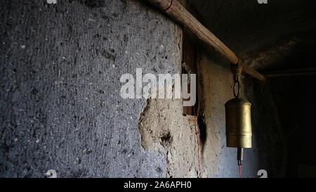 Der Traditionelle äthiopische Hirten messing Glocke gegen raue Felswand gehauen mit seitlicher Beleuchtung in Asheton Maryam Kloster, Lalibela, Äthiopien hängen Stockfoto