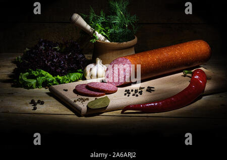 Geräucherter Salami auf einem alten Holztisch. Wurst mit Kräutern, Knoblauch und Pfeffer. Stockfoto