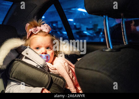 Ein hübsches kleines Mädchen mit rosey Wangen sitzt in einem Auto in Ihr Auto in einem Parkhaus Stockfoto